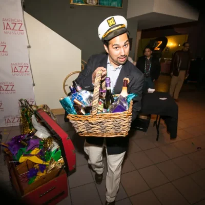 A man with a captain's hat carrying a gift basket of alcoholic beverages.